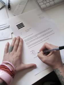 Tattooed and bangled hands writing a resignation letter