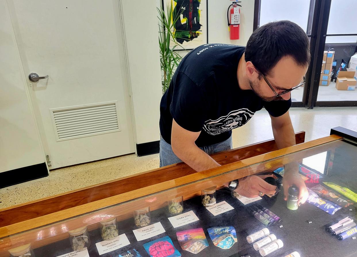 Budtender Mike Vogel adjusts some products beneath a glass display on Friday, April 26, 2024, at Moses Roses in Port Huron.