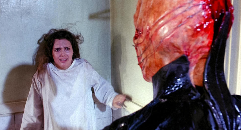 A terrified woman stares at a mutilated humanoid in leather