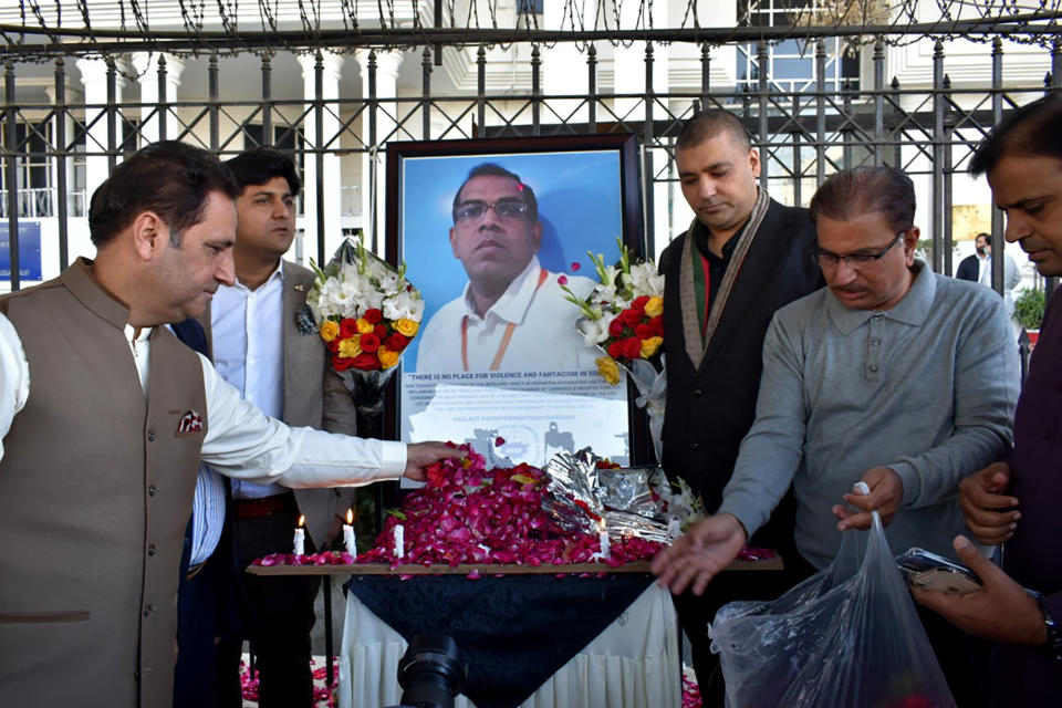 Businessmen put candles and rose petals next to the portrait of a Sri Lankan manager of a sports equipment factory, as they pay tribute to him outside the office of Sialkot Chamber of Commerce and Industry in Sialkot, Pakistan, Saturday, Dec. 4, 2021. Police arrested multiple suspects and detained dozens of others in the lynching of the Sri Lankan employee at the sports equipment factory in eastern Pakistan, officials said Saturday. (AP Photo/Shahid Ikram)