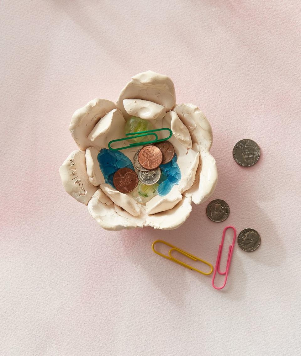 small flower shaped clay change bowl with child&#39;s signature inscribed in one petal holds dimes, pennies, and paper clips
