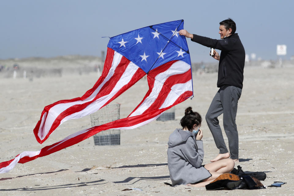 Stephen Wilmer, of Lindenhurst, N.Y., works at getting his kite aloft in the breeze as his daughter Emma adjusts her protective face mask as the family visited Jones Beach, in Wantagh, N.Y., Thursday, May 21, 2020, amid the coronavirus pandemic. As pandemic lockdowns ease across the United States, millions of Americans are set to take tentative steps outdoors to celebrate Memorial Day, the traditional start of summer. But public health officials are concerned that if people congregate in crowds or engage in other risky behaviors, the long weekend could cause the coronavirus to come roaring back. (AP Photo/Kathy Willens)