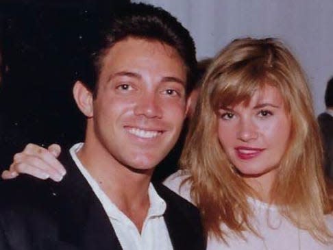 jordan belfort on the left wearing a black suit jacket and white button down, nadine on the right wearing a white dress with her arm around belfort