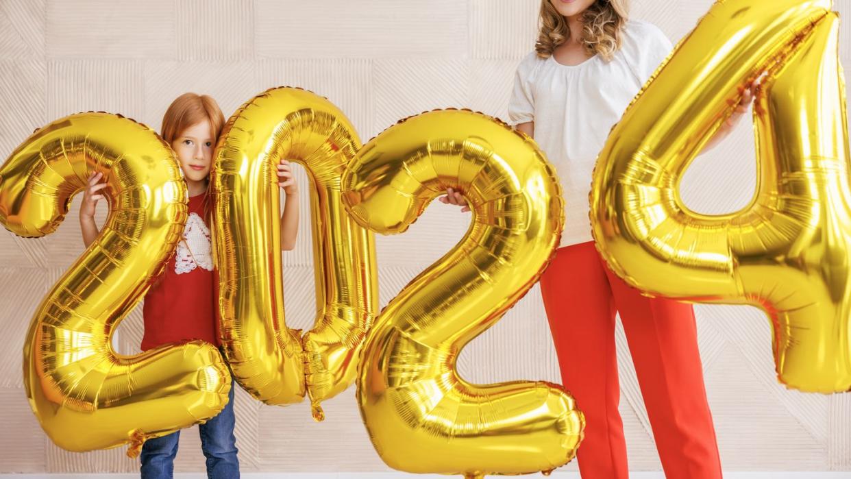 beautiful happy mother and daughter having fun decorating home for christmas, holding giant balloons shaped as numbers 2024 representing the upcoming new year