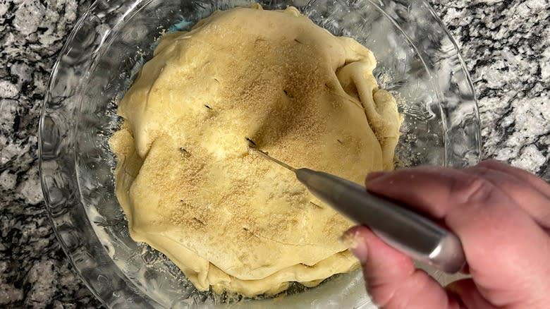 hand making slits in unbaked pie with knife