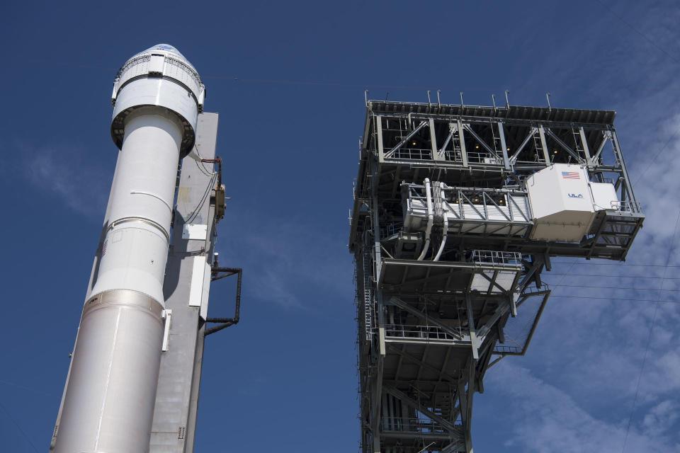 rocket with starliner spaceship atop next to launch tower against blue skies