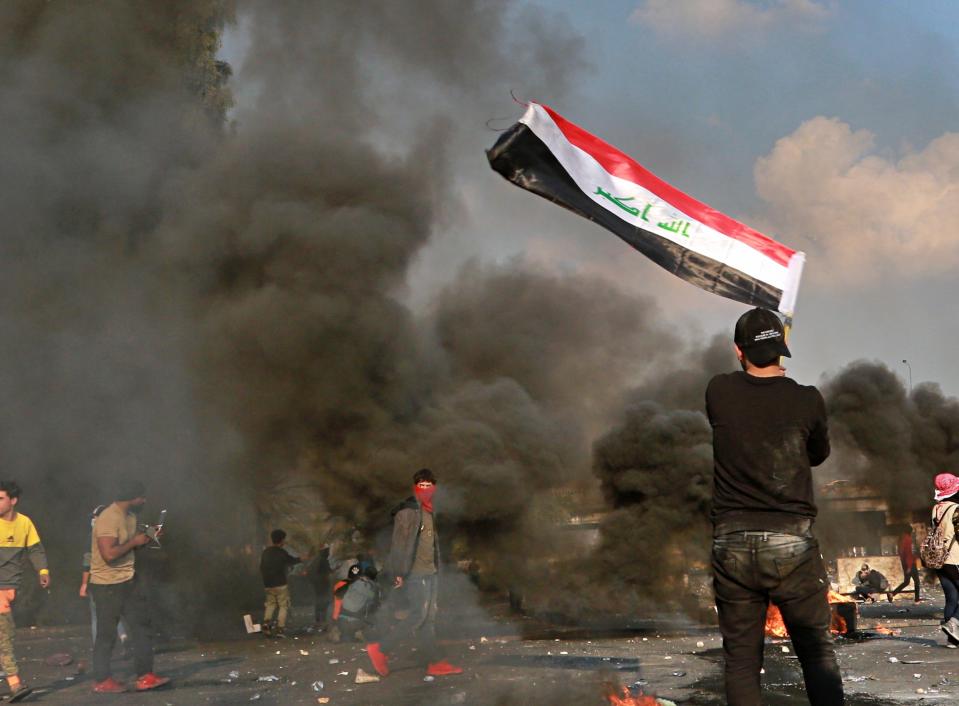 A protester waves the national flag during clashes with security forces in central Baghdad, Iraq, Monday, Jan. 20, 2020. Iraqi security forces also used live rounds, wounding over a dozen protesters, medical and security officials said, in continuing violence as anti-government demonstrators make a push to revive their movement in Baghdad and the southern provinces. (AP Photo/Hadi Mizban)