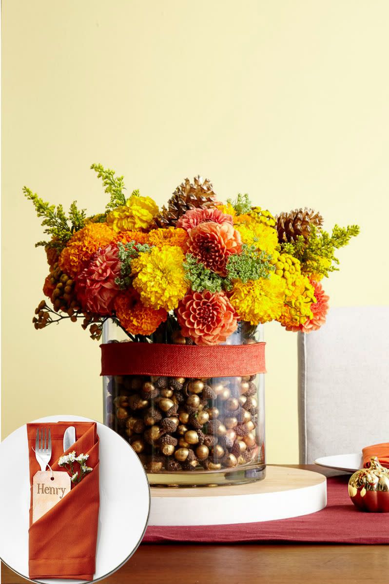 <p>To make this bountiful bouquet, first paint a few dozen acorns and three pinecones gold. Next, place a narrow round vase inside a wider one, and fill the gap with the acorns. Glue skewers to the pinecones, then arrange with fresh flowers in the smaller vase. Tie it all together with matching ribbon. </p><p>For the napkin shown: </p><p><strong>1.</strong> Lay the napkin flat to create a triple pocket fold. Fold in half vertically from right to left, then bring the bottom up to fold in half again. </p><p><strong>2</strong>. Fold the top layer of the upper left corner down to the bottom right corner. Repeat with the second and third layers, tucking the corners underneath each previous layer about 1½" to create the folds. </p><p><strong>3</strong>. Flip the napkin over to the back. Fold the right side back over a third of the napkin, then do the same with the left side. </p><p><strong>4. </strong>Flip back over to reveal the finished napkin.</p>