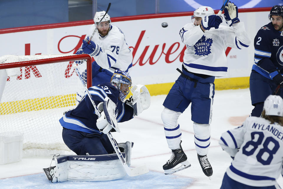 Toronto Maple Leafs' Nick Foligno (71) deflects the puck toward Winnipeg Jets goaltender Connor Hellebuyck (37) during the second period of an NHL hockey game Friday, May 14, 2021, in Winnipeg, Manitoba. (John Woods/The Canadian Press via AP)