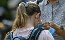 A student gets her face mask prepared by her mother at a school in Gelsenkirchen, Germany, Wednesday, Aug. 12, 2020. Students in North Rhine-Westphalia will have to wear face masks at all times due to the coronavirus pandemic as they return to school this Wednesday. (AP Photo/Martin Meissner)