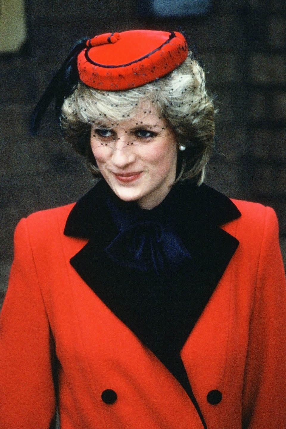 <p>In a bold black-and-red veiled cap.</p>