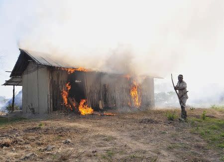 A tribal plantation worker holds a bow and arrow as he stands next to a burning house belonging to indigenous Bodo tribesmen after ethnic clashes in Balijuri village, in Sonitpur district in the northeastern Indian state of Assam December 24, 2014.REUTERS/Stringer