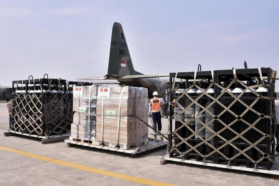 In this photo released by Indonesian Armed Forces, a military personnel stand guard near oxygen canisters and other relief goods unloaded from a Singaporean Air Force cargo plane at Halim Perdanakusuma Airbase in Jakarta, Indonesia, Friday, July 9, 2021. The world's fourth most populous country is running out of oxygen as it endures a devastating wave of coronavirus cases and the government is seeking emergency supplies from other countries, including Singapore and China. (Indonesian Armed Forces via AP)