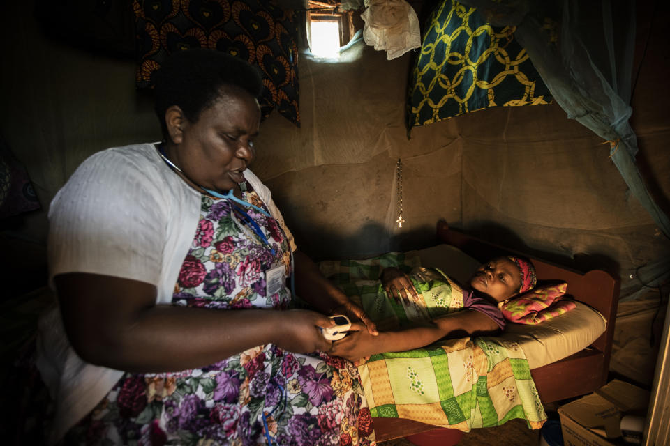 In this photo taken Tuesday, Nov. 5, 2019, palliative care nurse Madeleine Mukantagara, 56, left, uses a pulse-oximeter to check on the health of Vestine Uwizeyimana, 22, right, who has spinal degenerative disease and is taking oral liquid morphine for her pain, at her home in the village of Bushekeli, near Kibogora, in western Rwanda. While people in rich countries are dying from overuse of prescription painkillers, people in Rwanda and other poor countries are suffering from a lack of them, but Rwanda has come up with a solution to its pain crisis - it's morphine, which costs just pennies to produce and is delivered to households across the country by public health workers. (AP Photo/Ben Curtis)