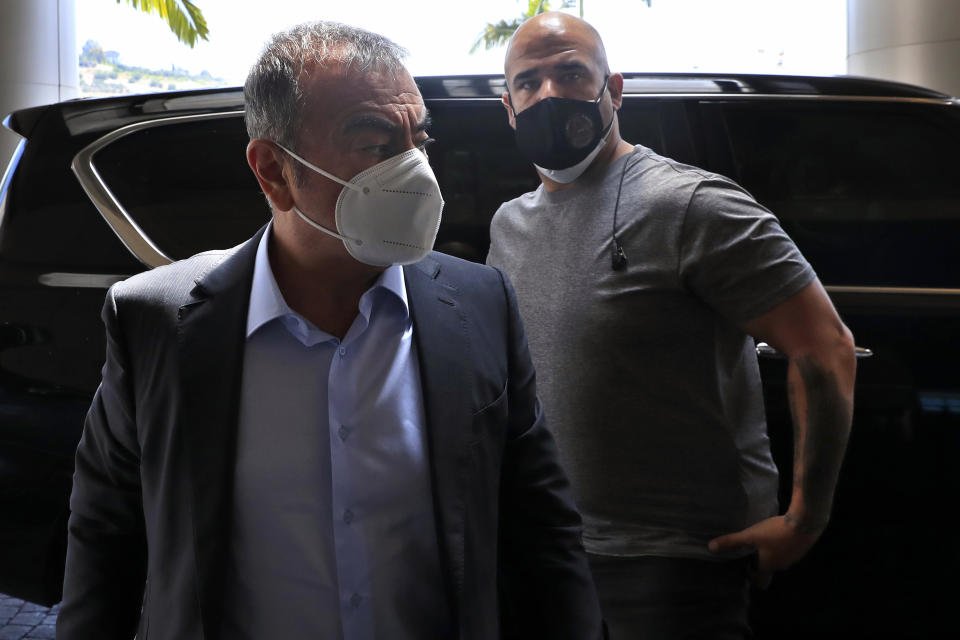 Fugitive ex-auto magnate Carlos Ghosn, foreground, steps out from a Nissan SUV, as he escorted by his bodyguard, as he arrived for an interview with The Associated Press, in Dbayeh, north of Beirut, Lebanon, Tuesday, May 25, 2021. The embattled former chairman of the Renault-Nissan-Mitsubishi alliance dissected his legal troubles in Japan, France and the Netherlands, detailed how he plotted his brazen escape from Osaka, and reflected on his new reality in crisis-hit Lebanon, where he is stuck for the foreseeable future. (AP Photo/Hussein Malla)