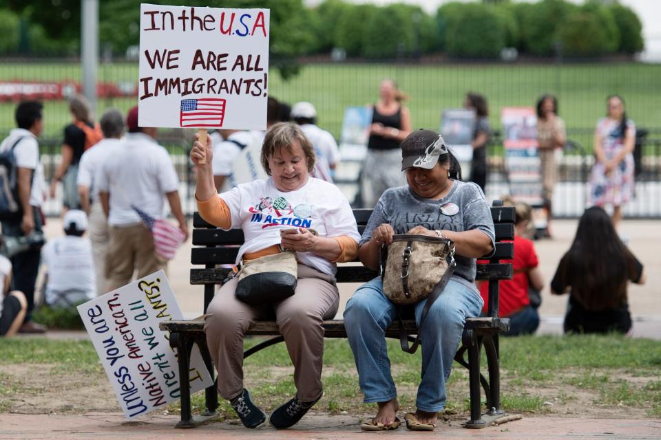 Two women with placards sit on a park bench as demonstrators with Casa in Action and Service Employee International Union 32BJ march in protest of Trump's immigration policies in Washington, D.C., May 1, 2017.