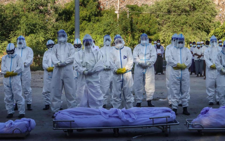 Volunteers wearing personal protective equipment (PPE) pray in front of bodies of people who died from the Covid-19 coronavirus during their funeral at a cemetery in Mandalay on July 14, 2021.  - AFP