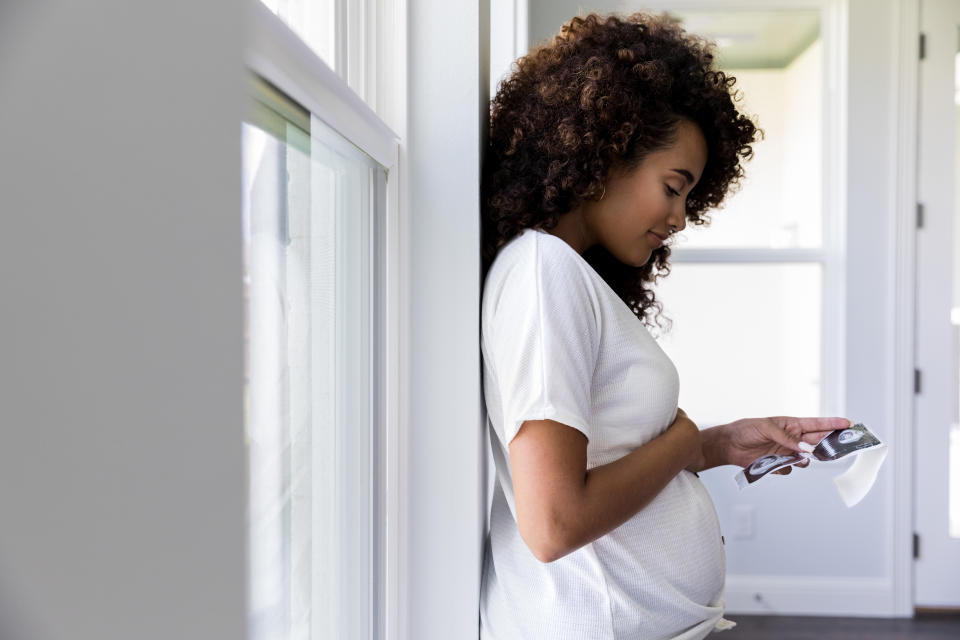 A profile view of a pregnant mid adult woman looking at the ultrasound photos of her baby.