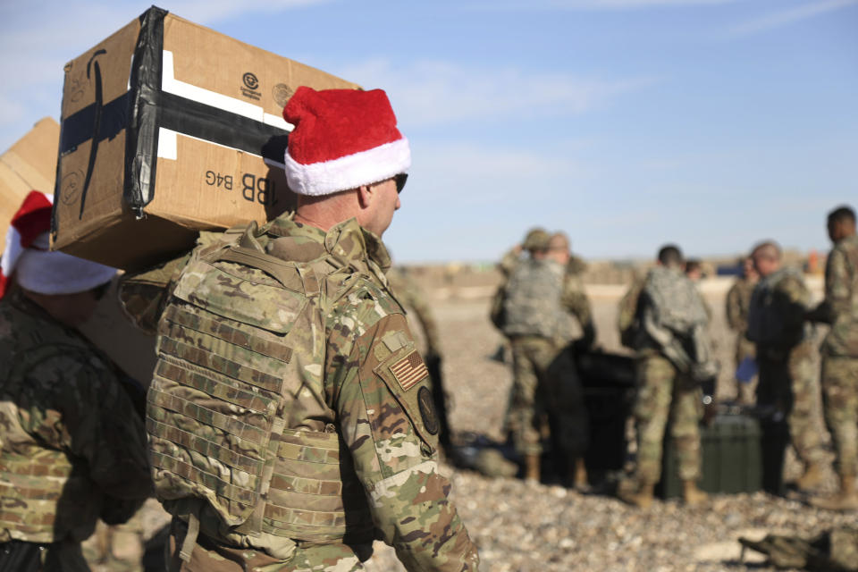 In this Monday, Dec. 23, 2019, photo, a U.S. soldier carries Christmas gifts from a helicopter to deliver to his comrades on a base near the al-Omar oilfield in eastern Syria. It's an operation is called Holiday Express - in addition to delivering presents, the U.S.-led coalition forces brought a U.S. military band to play Christmas carols and music to several bases in eastern Syria. (AP Photo/Farid Abdul-Wahid)