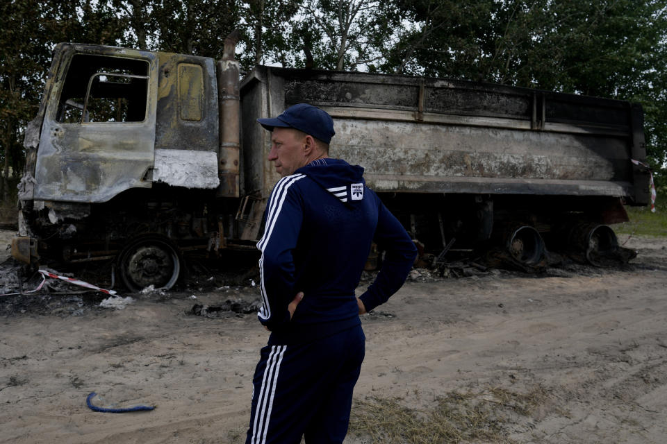 Vadym Schvydchenko stands next to his truck recently damaged by a mine on a dirt track near Makariv, on the outskirts of Kyiv, Ukraine, Tuesday, June 14, 2022. The detonation of the 7.5-kilogram (16-pound) explosive charge blew Vadym Schvydchenko and his daughter's toy clean out of the cabin. The truck — and his livelihood — went up in flames. (AP Photo/Natacha Pisarenko)