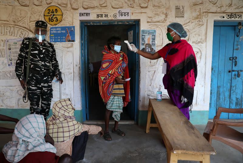 A woman checks the temperature of a voter before he casts his vote at a polling booth in Purulia