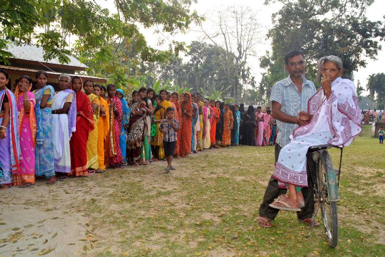 An elderly Indian voter, seen sitting on her son's bicycle, gestures her inked-marked finger as others wait in line to vote outside a polling station in Koliabor, in Assam state's Nagaon district some 180 kms east of Guwahati, on April 7, 2014