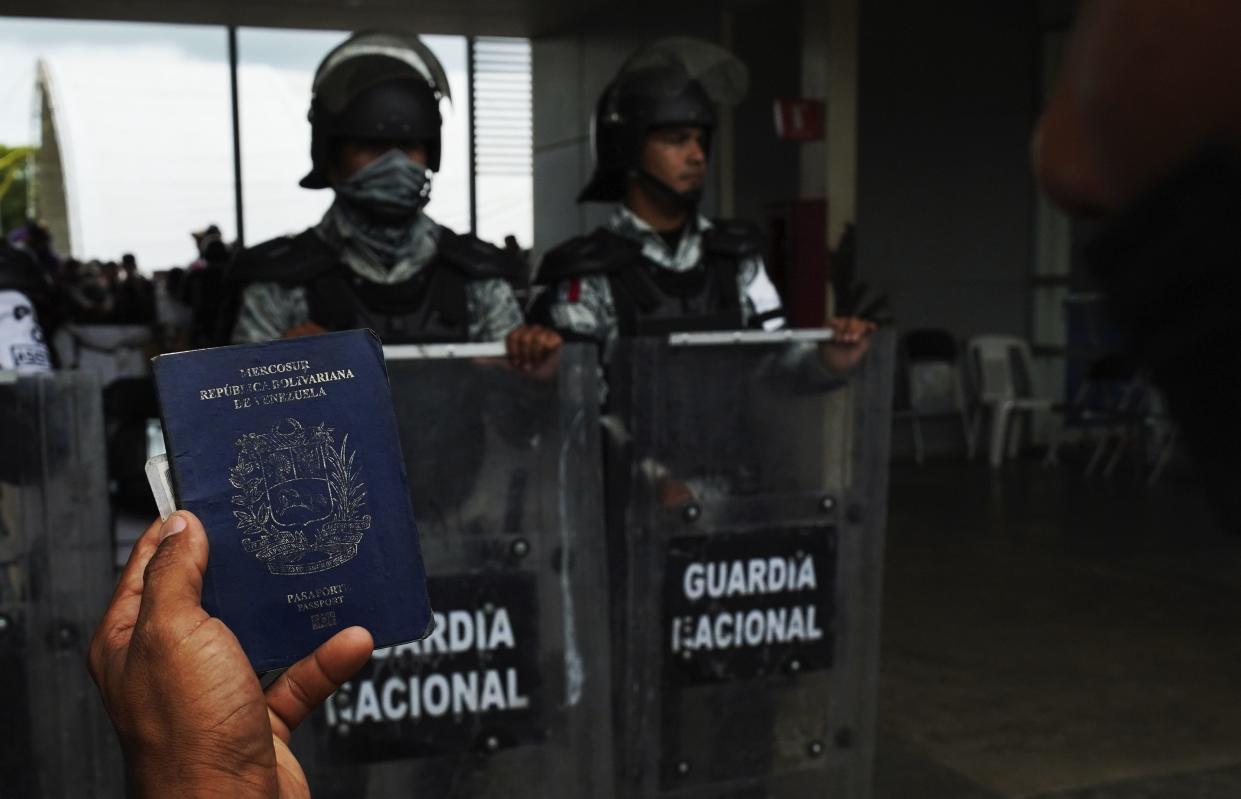 A migrant holds up his Venezuelan passport outside the Border Transit Comprehensive Care Center, guarded by National Guards, to ask for legal documents that allow his group to travel through Mexico, on the outskirts of Huixtla, Mexico, on June 10, 2022.