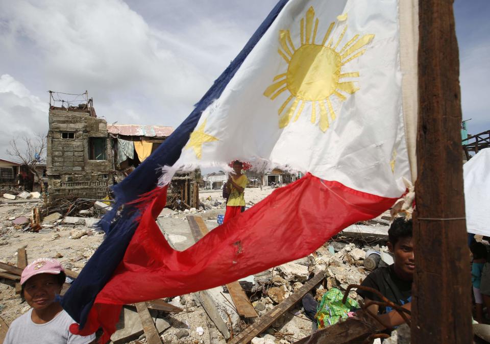 Typhoon victims wait for relief supplies near a tattered Philippine flag in Hernani, Samar, that was hit by super Typhoon Haiyan in central Philippines