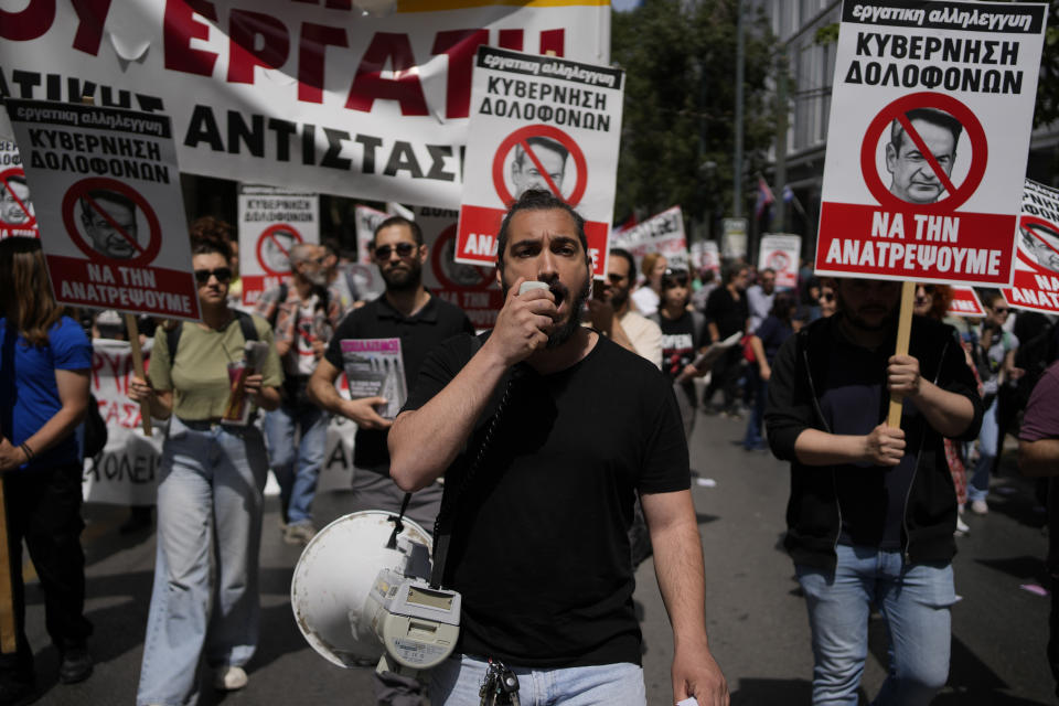 A protester using a loudspeaker shouts slogans during a rally in Athens, Greece, Wednesday, April 17, 2024. A 24-hour strike called by Greece's largest labor union have halted ferries and public transport services in the Greek capital and other cities, to press for a return of collective bargaining rights axed more than a decade ago during a severe financial crisis. Writing on banner with red line across the face of Greece’s Prime Minister, Kyriakos Mitsotakis, reads in Greek; “Killer Government / We Will Overturn It”. (AP Photo/Thanassis Stavrakis)