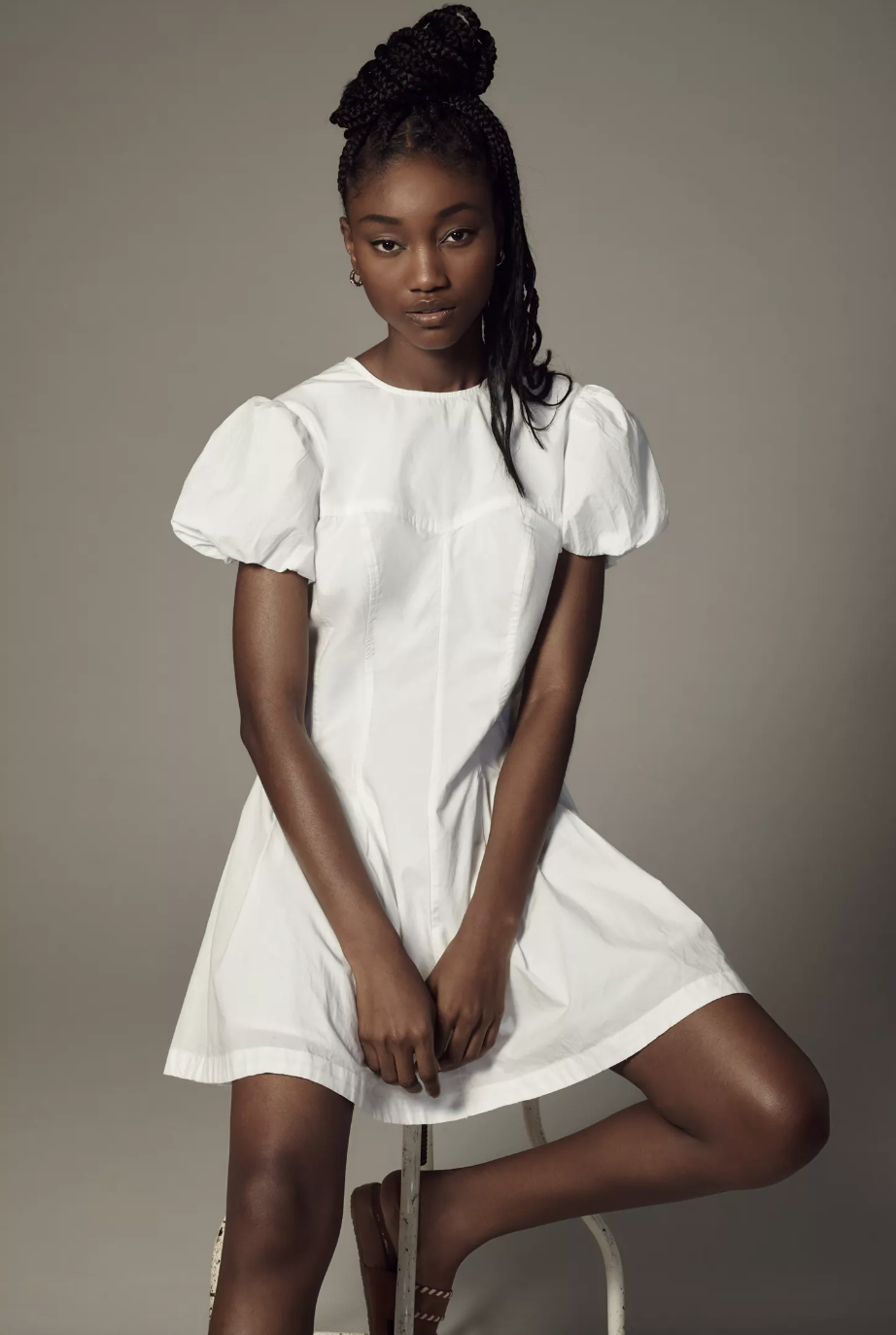 model sitting on stool wearing white mini dress, Maeve Puff-Sleeve Pleated Dress (photo via Anthropologie)