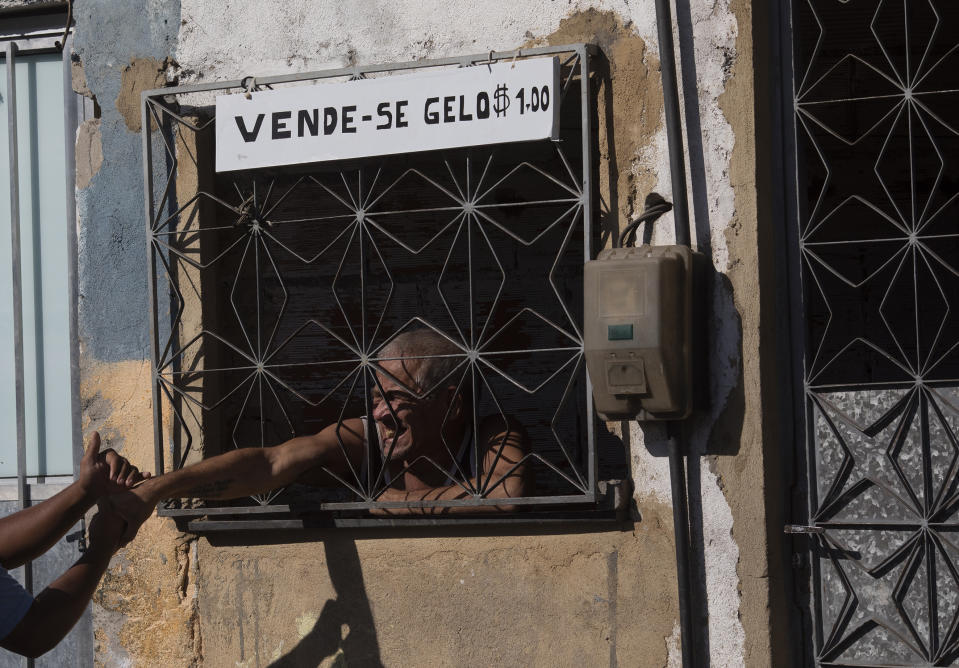 A resident greets a water utility worker from CEDAE through his home's window, where he has a sign that reads in Portuguese "Ice for sale," as water workers disinfect the Mare Complex slum in an effort to curb the spread of the new coronavirus, in Rio de Janeiro, Brazil, Monday, May 4, 2020. (AP Photo/Silvia Izquierdo)