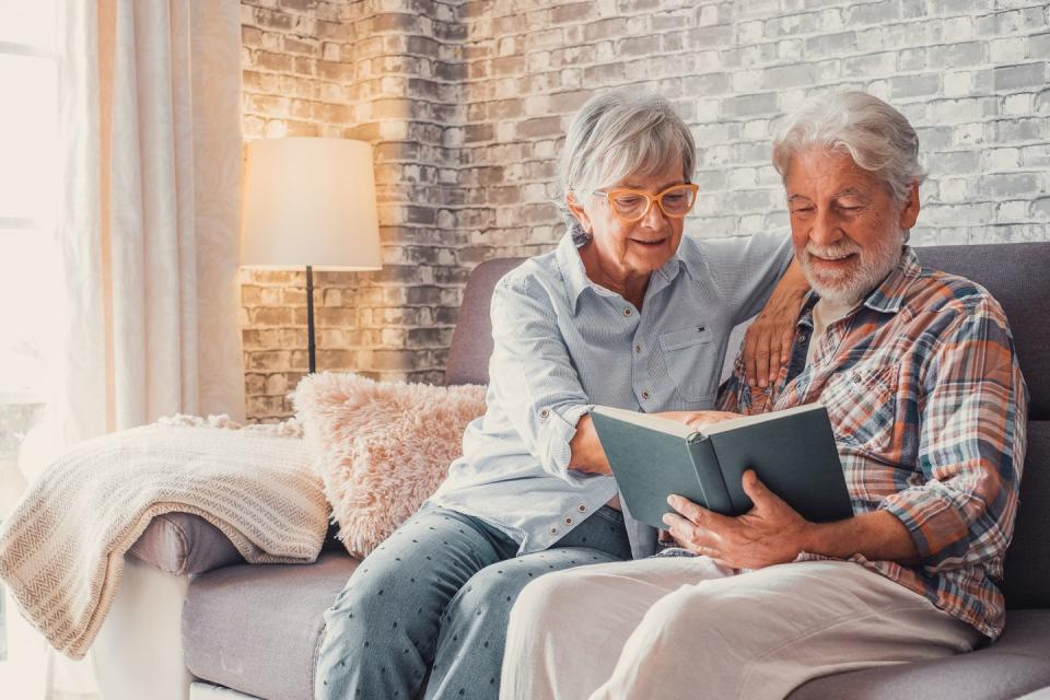 portrait of couple of two cute grandparents reading a book together sitting on the sofa grandmother and grandfather relaxing weekend on free time