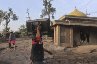 A man carries a television as he walks past a mosque partially buried in volcanic ash from the eruption of Mount Semeru in Kajar Kuning village in Lumajang, East Java, Indonesia, Monday, Dec. 5, 2022. Indonesia's highest volcano on its most densely populated island released searing gas clouds and rivers of lava Sunday in its latest eruption. (AP Photo/Imanuel Yoga)