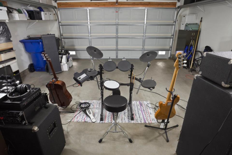 Music equipment, including amps, guitars, and a drum set, set up in a garage.