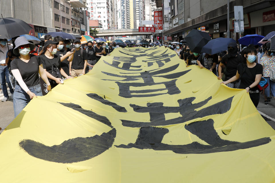 Masked protesters walk next to a banner with the words "May Glory be to Hong Kong" in Hong Kong on Saturday, Oct. 5, 2019. All subway and trains services are closed in Hong Kong after another night of rampaging violence that a new ban on face masks failed to quell. (AP Photo/Vincent Thian)