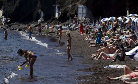 Tourists sunbathe on the Red Beach on the Greek island of Santorini, Greece, July 2, 2015. REUTERS/Cathal McNaughton