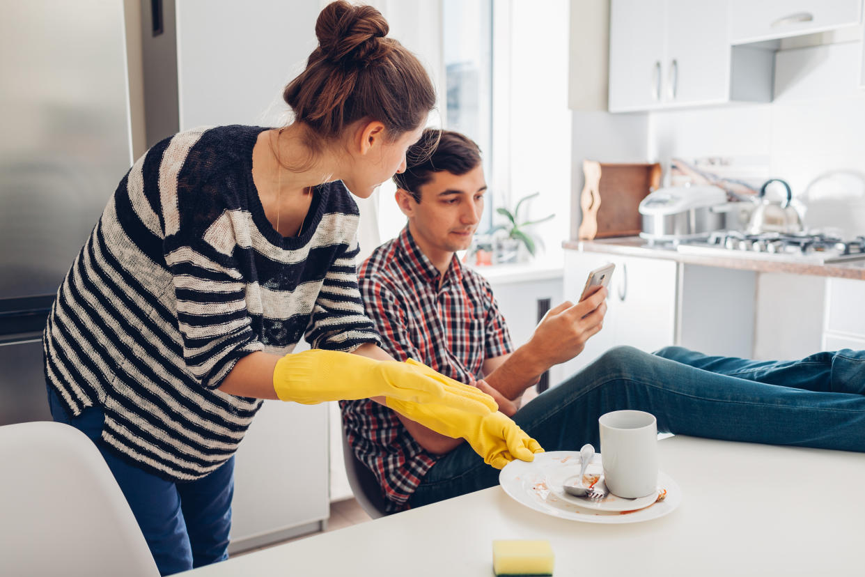 Lazy boyfriend hanging in phone while his girlfriend cleaning his dishes after dinner in kitchen. Inequality of men's and women's rights. Family arguement