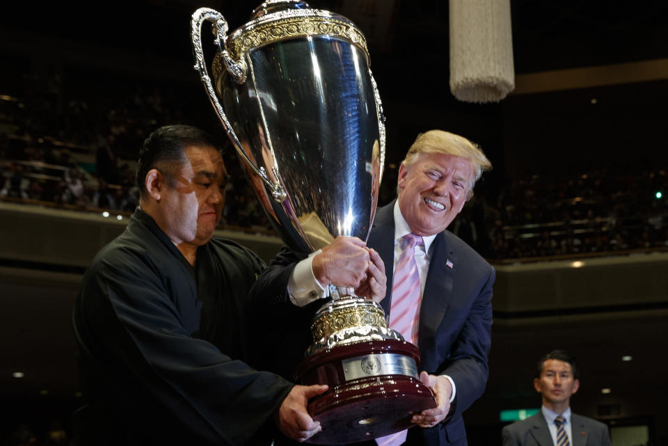 President Donald Trump lifts the "President's Cup" to present to Tokyo Grand Sumo Tournament winner Asanoyama, at Ryogoku Kokugikan Stadium, Sunday, May 26, 2019, in Tokyo. (AP Photo/Evan Vucci)