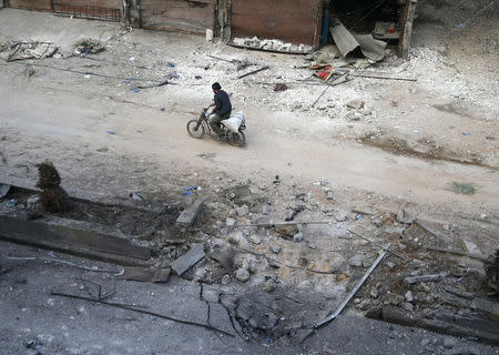 A man rides on a motorbike at a damaged site in the rebel held besieged town of Hamouriyeh, eastern Ghouta, near Damascus, Syria, February 21, 2018. REUTERS/Bassam Khabieh