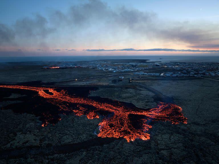 Se ven explosiones de lava y humo que se eleva cerca de edificaciones residenciales en la ciudad suroccidental islandesa de Grindavik después de una erupción volcánica el 14 de enero de 2024. 