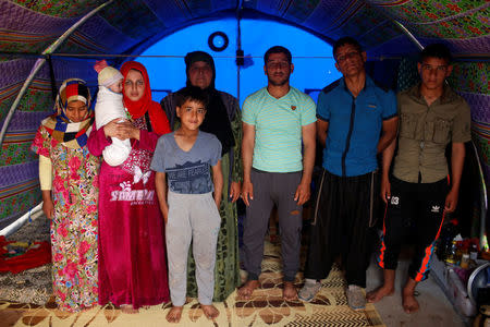 Displaced Iraqi woman Farah Taha, 60, poses for a photograph with her three sons, her daughter-in-law, her six-month-old grandchild as well as the brother and sister of her daughter-in-law, in the family tent in Hammam al-Alil camp south of Mosul, Iraq March 29, 2017. Taha says she has been unable to find any work to support her family since fleeing their Mosul home. REUTERS/Suhaib Salem