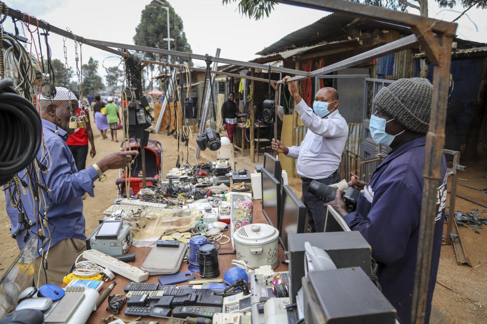 Onesmus Mauta, center, and Masumba, right, wear masks as they speak to a client, left, at their secondhand electronics street stall in the Kibera neighbourhood of Nairobi, Kenya Friday, March 20, 2020. For most people, the new coronavirus causes only mild or moderate symptoms such as fever and cough and the vast majority recover in 2-6 weeks but for some, especially older adults and people with existing health issues, the virus that causes COVID-19 can result in more severe illness, including pneumonia. (AP Photo/Patrick Ngugi)