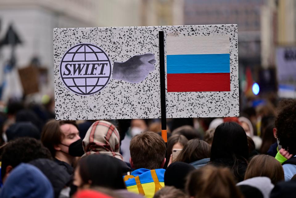 Supporters of the Fridays for Future movement hold a sign with the logo of bank messaging system SWIFT and the Russian flag during a demonstration against the war in Ukraine on March 3, 2022 in Berlin. (Photo by John MACDOUGALL / AFP) (Photo by JOHN MACDOUGALL/AFP via Getty Images)