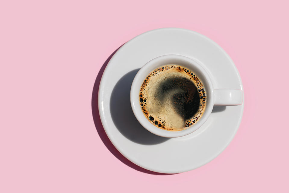 Directly Above Shot of fresh coffee on pastel pink color background. Coffee in white cup and plate. Espresso, black coffee. Nice choice for breakfast or take a break for coffee. Close-up. Copy space. Flat lay.