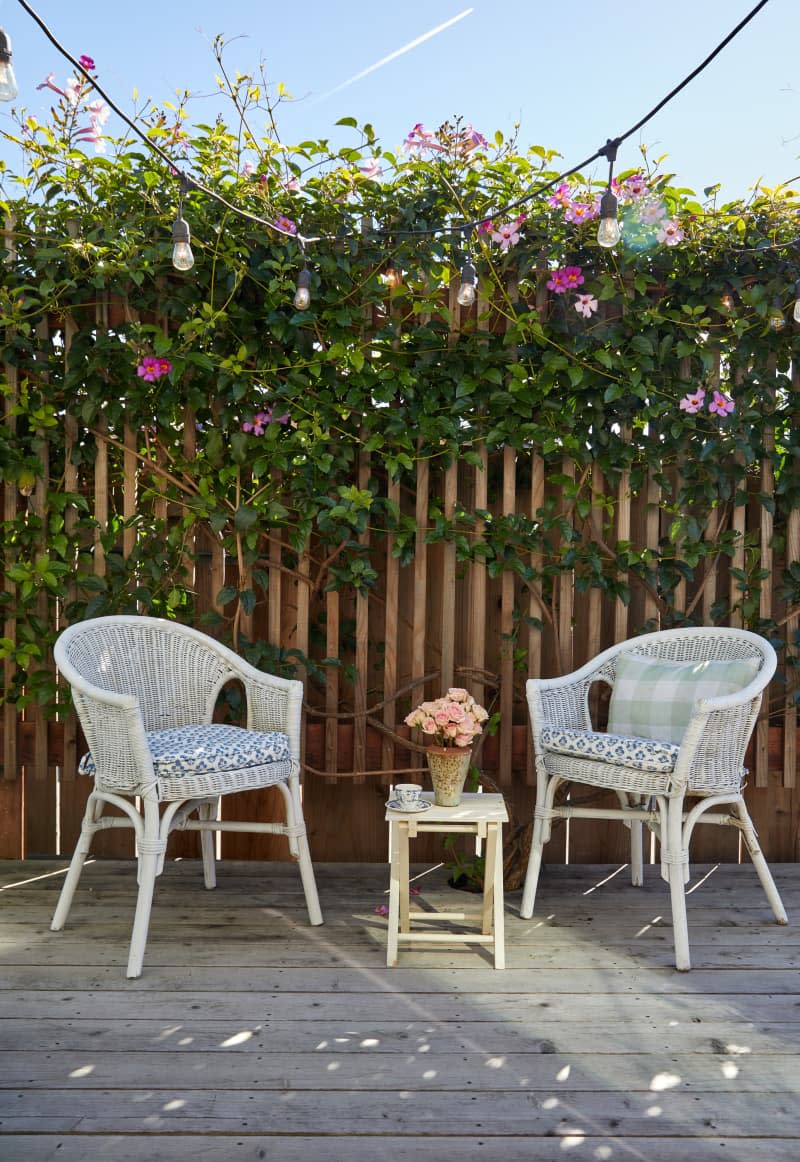Two chairs flank a small tea table with flowers in an outdoor space.