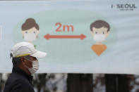 A man wearing a face mask as a precaution against the coronavirus walks past a banner showing social distancing at a park in Seoul, South Korea, Tuesday, Nov. 24, 2020. Authorities in the South Korean capital on Monday announced a tightening of social distancing regulations, including shutting nightclubs, limiting service hours at restaurants and reducing public transportation. (AP Photo/Lee Jin-man)