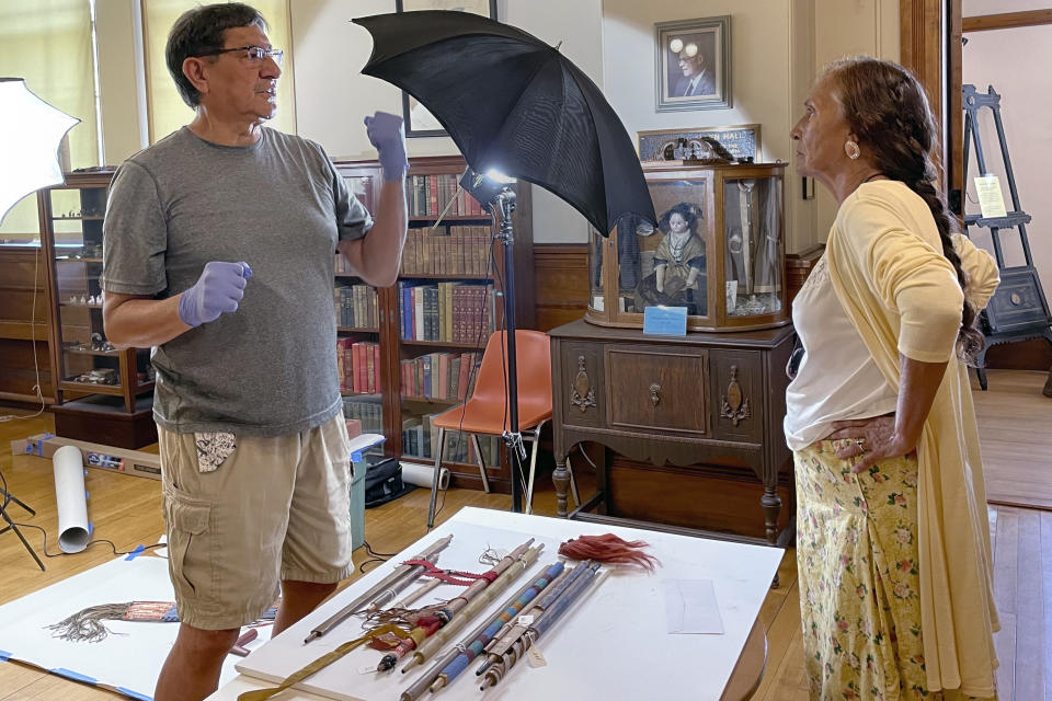 Leola One Feather, right, of the Oglala Sioux Tribe in South Dakota, talks with Jeffrey Not Help Him, left, also an Oglala Sioux tribe member, while Native American artifacts are photographed on July 19, 2022, at the Founders Museum in Barre, Massachusetts. The private museum, which is housed in the town library, is working to repatriate as many as 200 items believed to have been taken from Native Americans massacred by U.S. soldiers at Wounded Knee Creek in 1890. (AP Photo/Philip Marcelo)