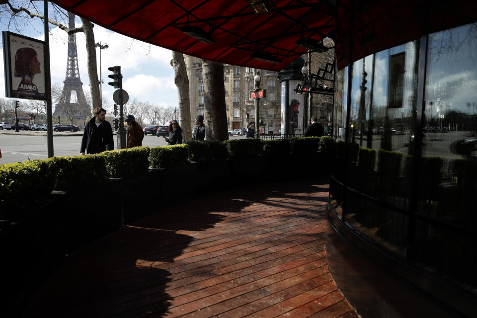 People look at an empty terrasse in Paris, Sunday, March 15, 2020. French Prime Minister Edouard Philippe announced that France is shutting down all restaurants, cafes, cinemas and non-essential retail shops, starting Sunday, to combat the accelerated spread of the virus in the country. For most people, the new coronavirus causes only mild or moderate symptoms. For some it can cause more severe illness. (AP Photo/Christophe Ena)