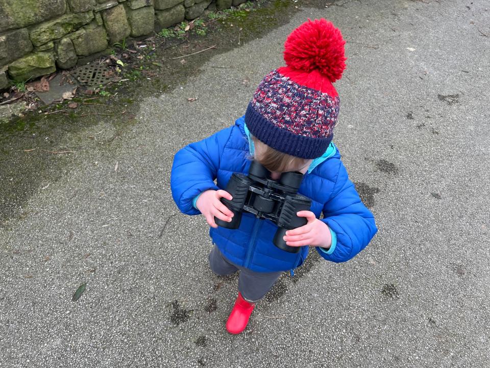 Jennifer Sizeland's son wearing a beanie and blue jacket while holding binoculars.