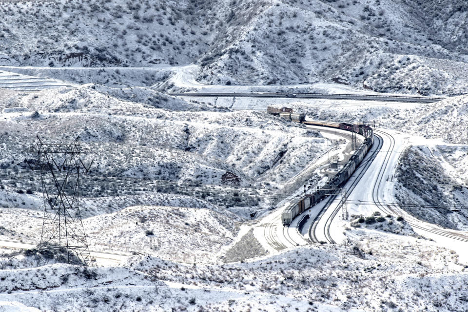 A train rolls along the snow covered hills in the Cajon Pass near Highway 138 in Phelan, Calif., Thursday, Feb. 21, 2019. (Watchara Phomicinda/The Orange County Register via AP)